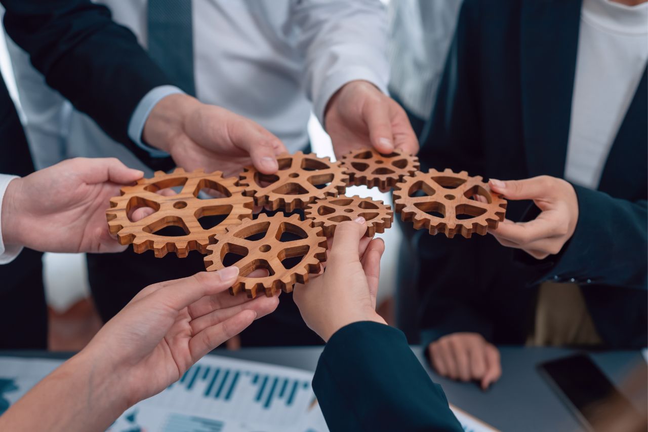 Kilka osób trzymających drewniane koła zębate ułożone razem